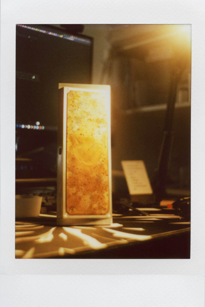 Warm amber-lit custom keyboard with translucent keycaps backlit by a glowing panel beside dim office equipment