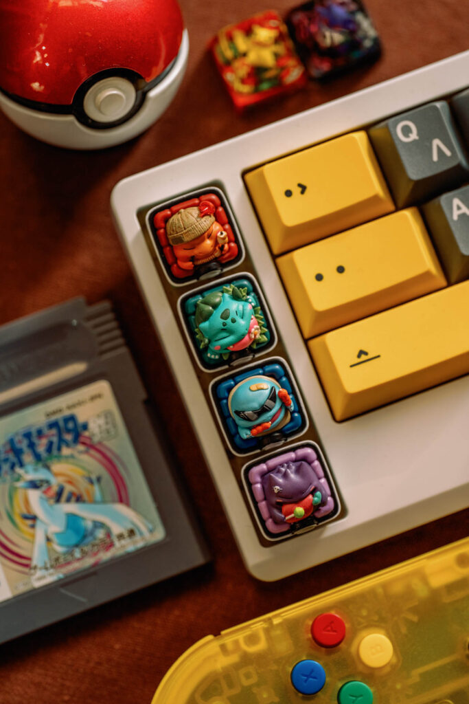 White custom keyboard with four sculpted character keycaps and yellow keys beside a Poke Ball on a desk