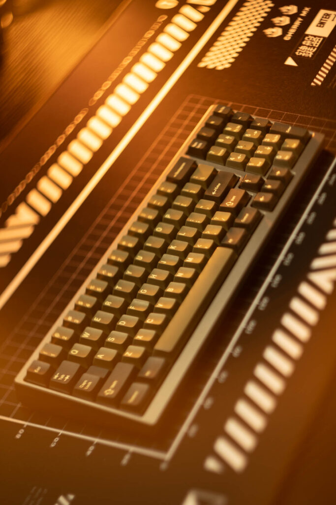 Dark compact mechanical keyboard with black keycaps on a grid-lined surface under warm amber light